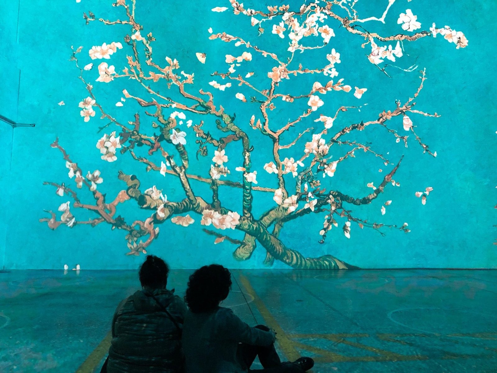 People sitting on a floor looking at Almond Blossom painting at Immersive Van Gogh Exhibit